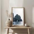 Framed artwork of a coastal scene on a wooden table with decorative items.