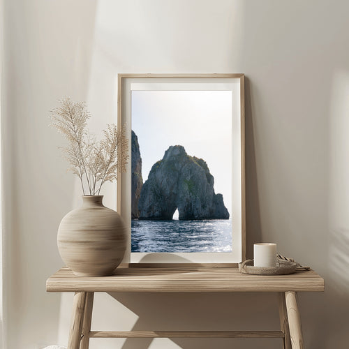 Framed artwork of a coastal scene on a wooden table with decorative items.